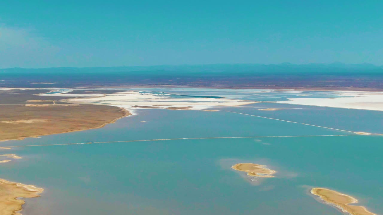 At 0:02, the Guerrero Negro aerial shows turquoise water filling most of the frame, with white salt flats across the far shore, small sandy islands low in frame, and no visible people.