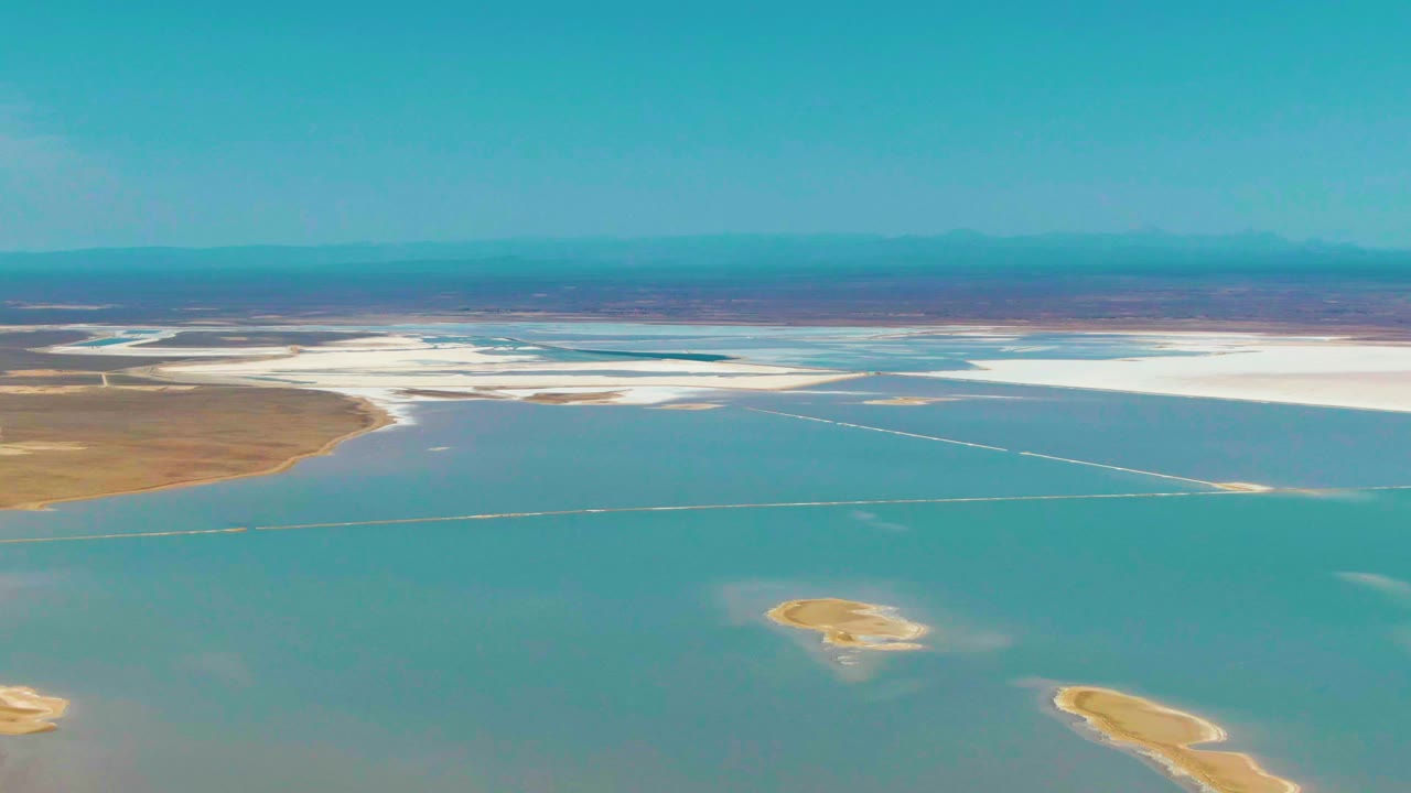 Aerial view of blue shallow water, white salt flats, brown land, and small islands.