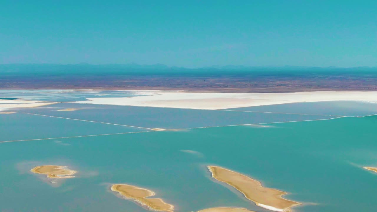 Aerial shot of shallow teal water, exposed tan lake bed, white flats, and distant mountains.