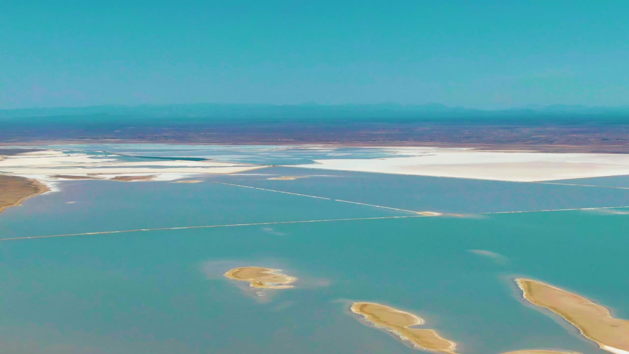 Aerial salt-flat landscape with turquoise water, white shore deposits, and tan sandbars in foreground.