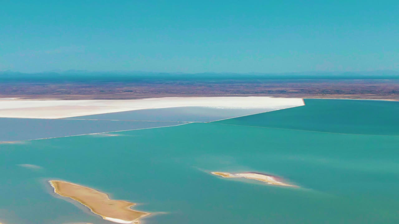 Aerial view in Guerrero Negro, Baja California Sur, showing turquoise water meeting a bright white salt flat, with tan sand islands in the foreground and no visible people.
