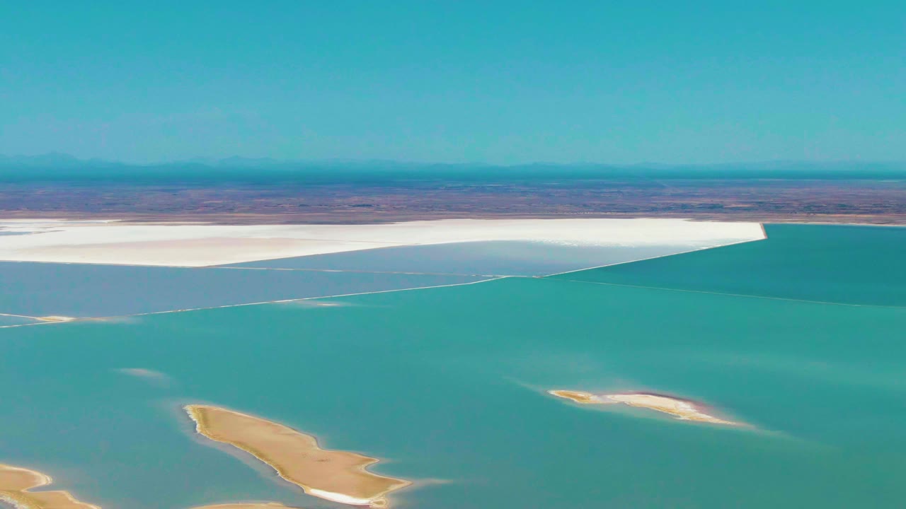 Turquoise lagoon water with pale sandy islands below a white salt flat and blue sky.