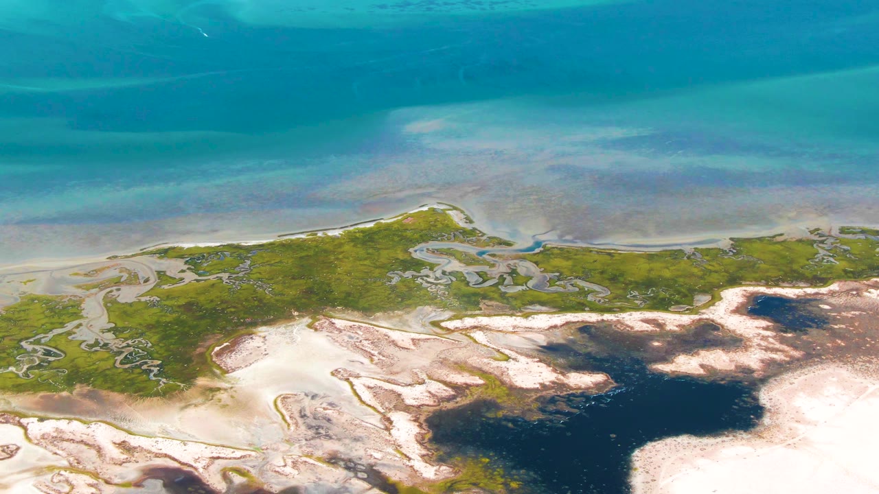 Aerial view of turquoise water, green marsh, pale sand, and dark tidal pools.