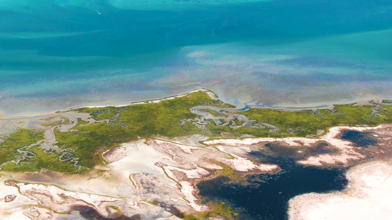 Second frame of the Guerrero Negro wetland shows shallow turquoise water above a green marsh band, with pale sand and dark tidal water below and no visible people.