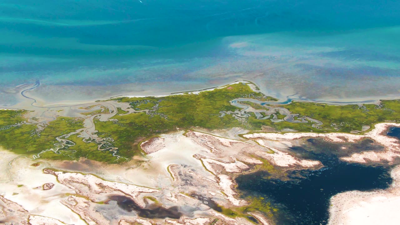 Aerial view of turquoise water, green marsh, pale sand, and dark tidal pools.