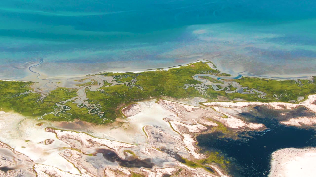 Overhead frame from Guerrero Negro, Baja California Sur, showing a green wetland strip, pale sandbars, muddy patches, and a dark blue coastal water pool with no visible people.