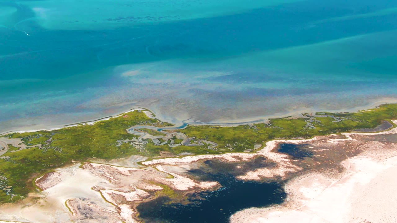 Overhead coastal wetland with turquoise water, green marsh, sand flats, and dark tidal pools.