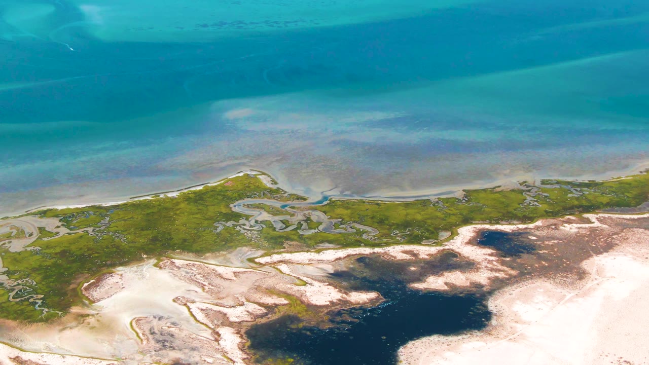 Guerrero Negro aerial view with turquoise shallows, thin shoreline, green wetland, pale sand flats, darker tidal water, and no visible people.