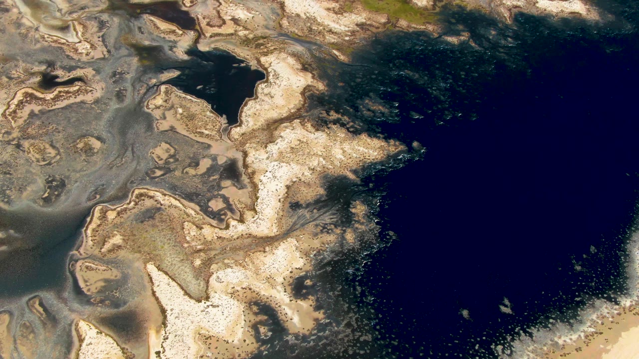Aerial view in Guerrero Negro with beige tidal flats, green-brown shallows, a small dark inlet near the upper left, and no visible people.