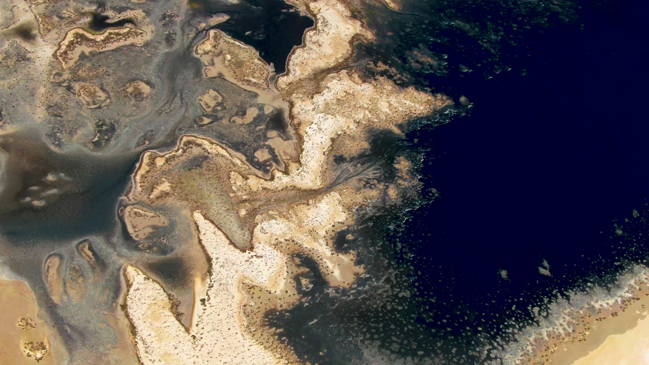 Aerial frame in Guerrero Negro, Baja California Sur, with cream sand islands, darker wet flats, a foamy water edge, and no visible people.