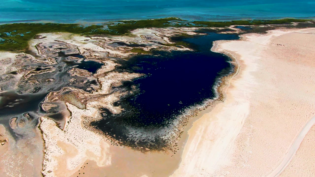 Aerial view of dark lagoon water beside pale sand and mudflats