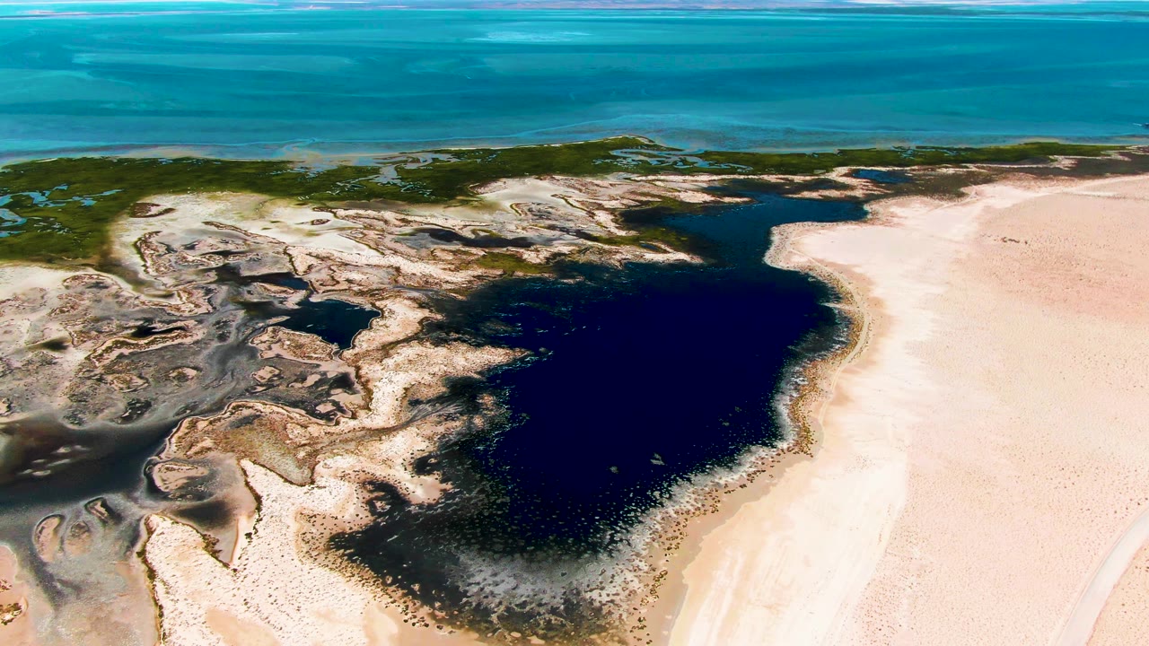 Wide aerial of lagoon and sandy shoreline with ocean in the distance.