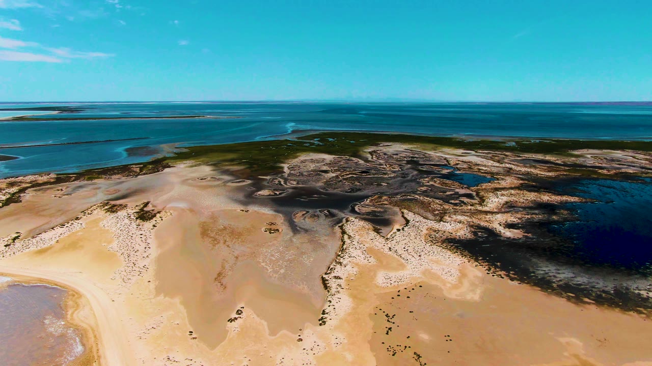 Aerial view in Guerrero Negro showing shallow tidal water tracing through light sand, darker pooled areas to the right, open sea beyond, and no visible people.