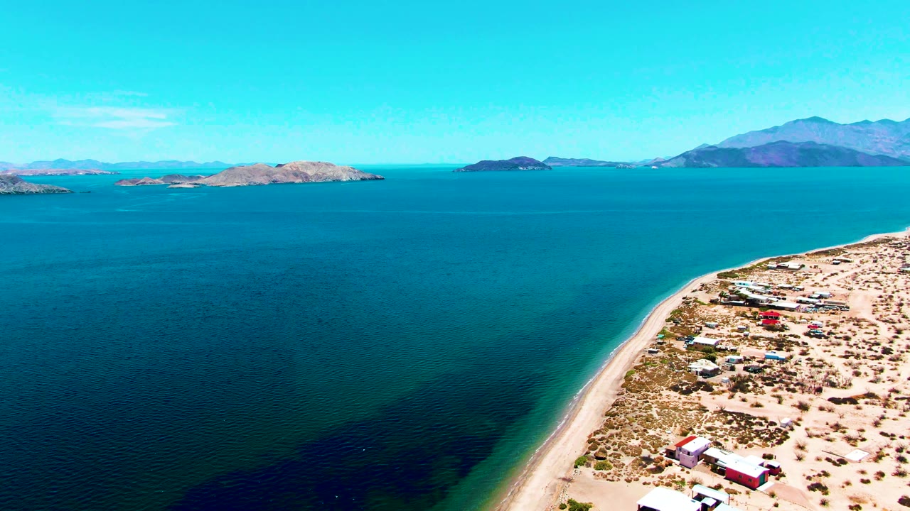 High aerial view of calm water and sandy coastline with small structures near shore.