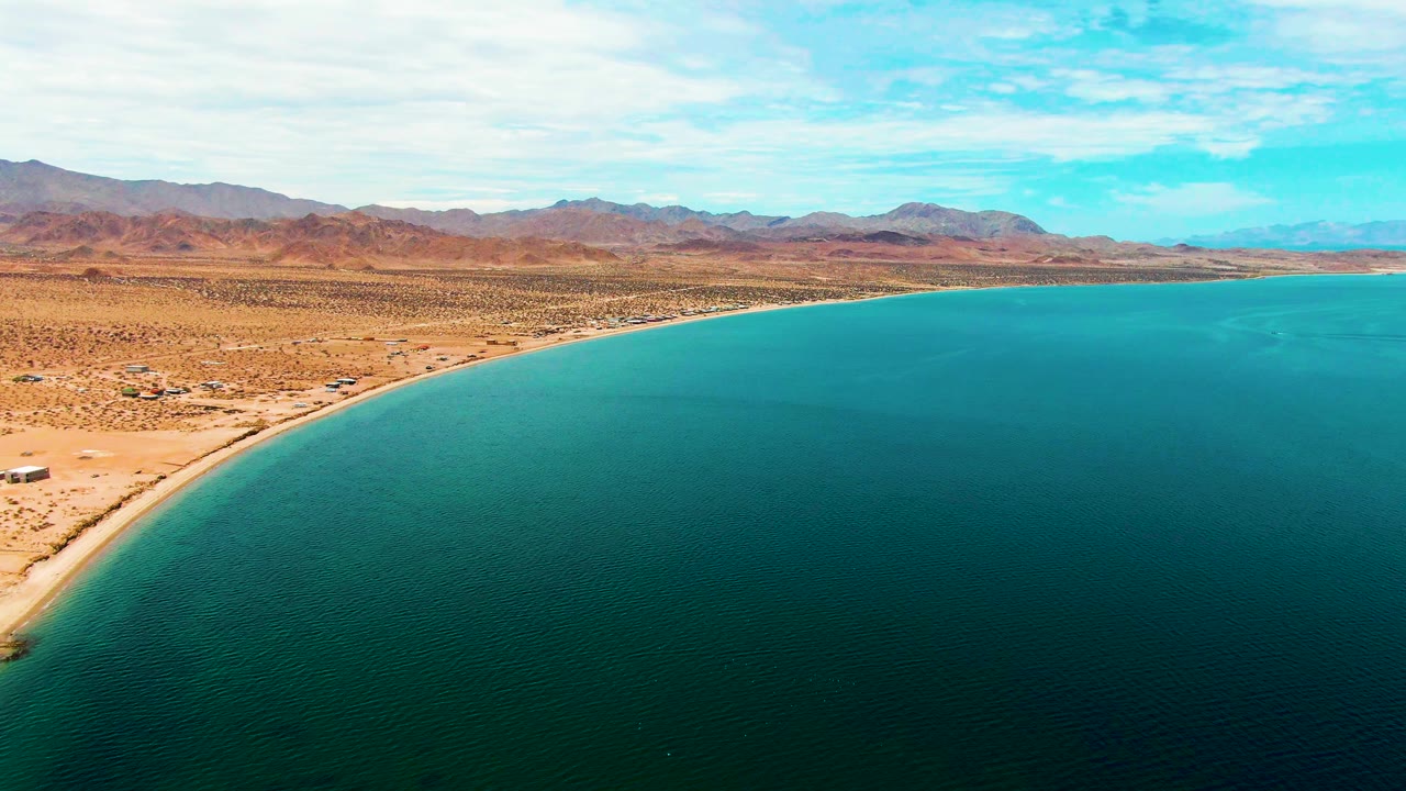 Desert beach and bay water viewed from above with mountains beyond.