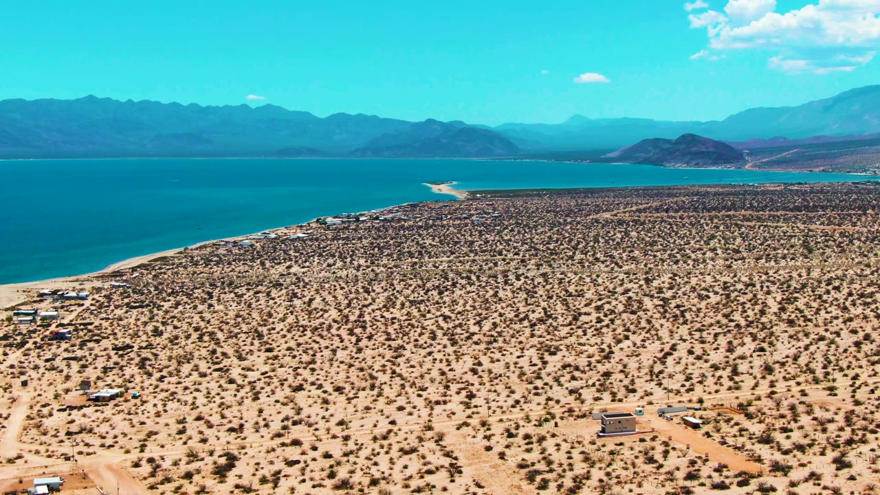 Aerial view of sandy desert foreground and blue water near mountains.