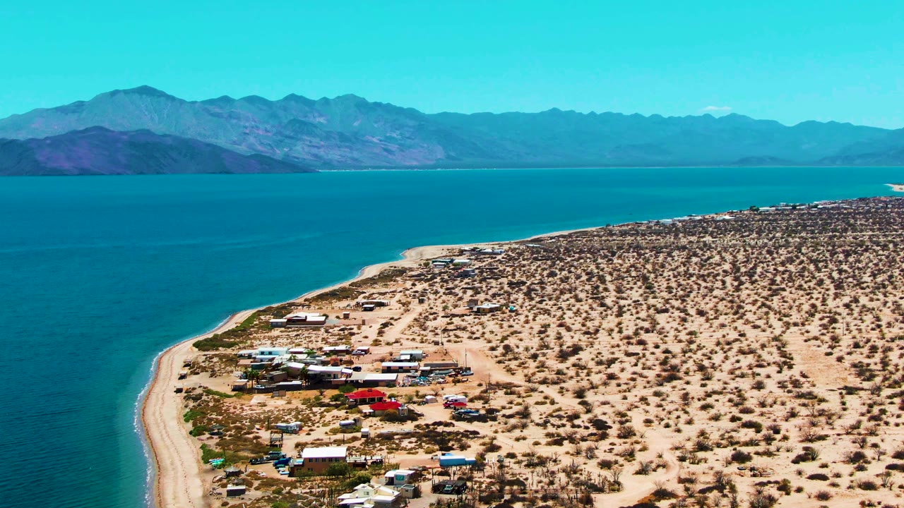Desert shoreline camp with vehicles near bright blue water.
