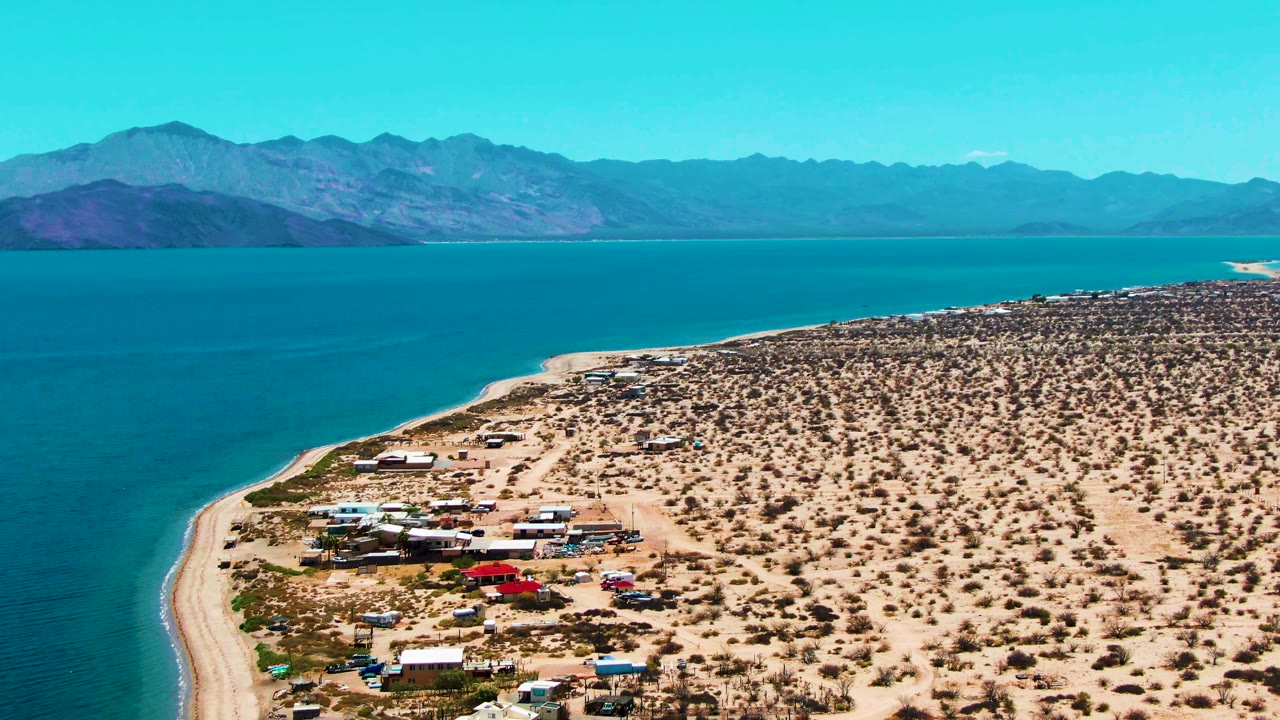 The third frame holds a broad Bahia De Los Angeles coastal view, placing the camp and red vehicle below the desert flats, with blue water and layered mountains beyond, and no visible people.