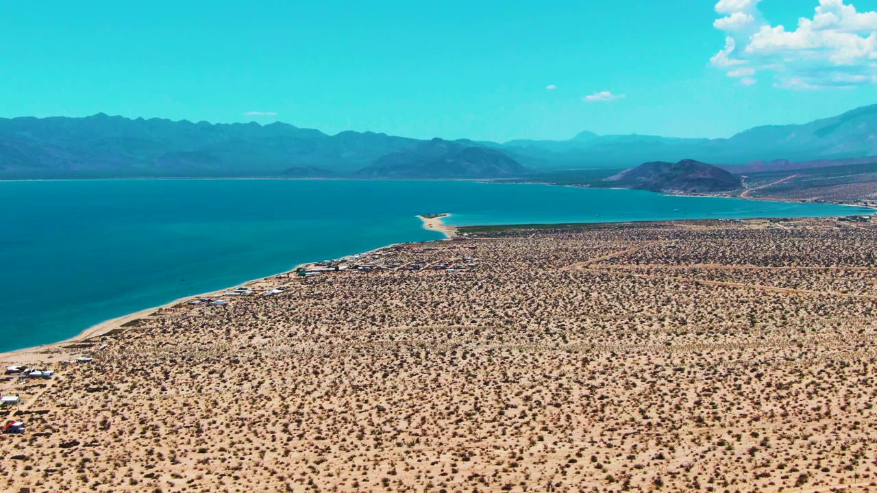 Aerial desert coast with bay water, sandy edge, and mountains.