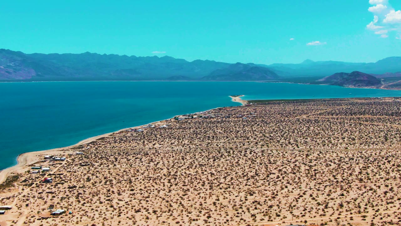 Aerial desert coast with turquoise water and mountains under clear sky.