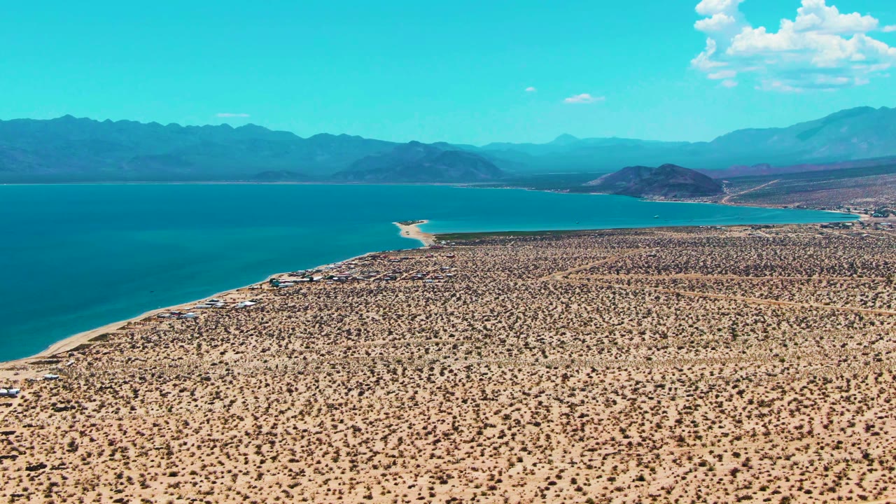 Aerial desert shoreline with blue water and distant mountains