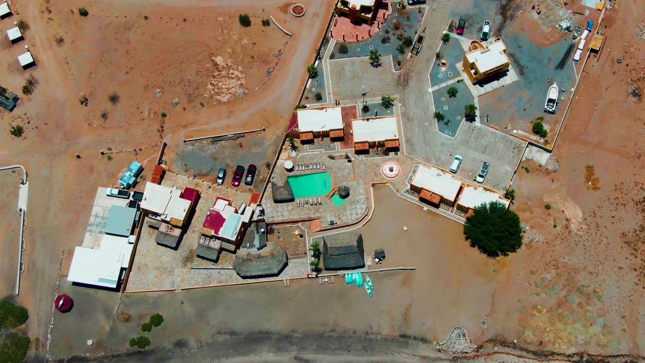 Aerial view of desert homes, dirt lots, pool, and road edges.