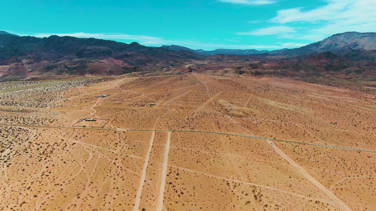 Aerial frame over Bahia De Los Angeles with sandy desert roads crossing the foreground, mountain ridges in the distance, bright sky, and no visible people.