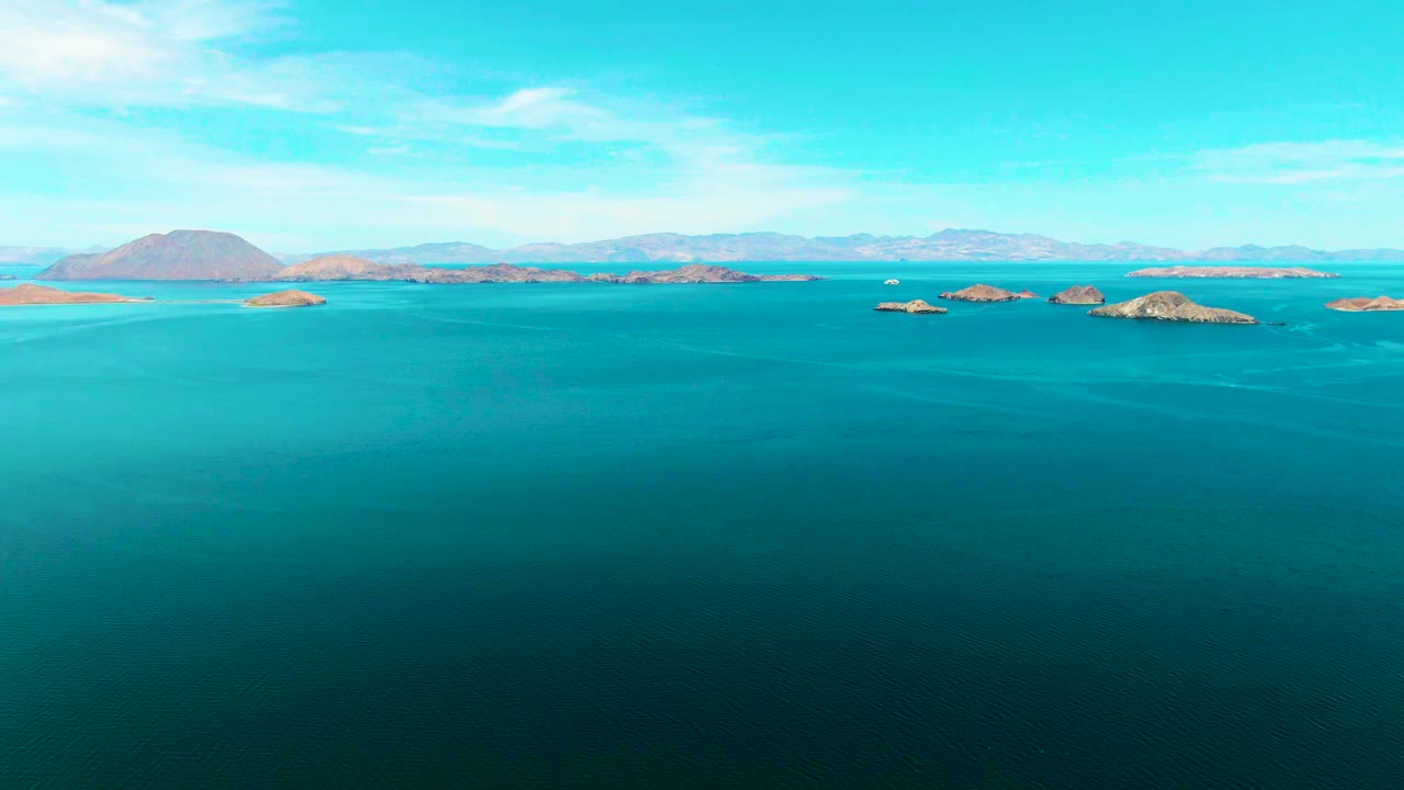 At two seconds, the frame shows an uninterrupted ocean foreground, clustered rocky islands near the horizon, a low mountain ridge in the background, bright sky, and no visible people.