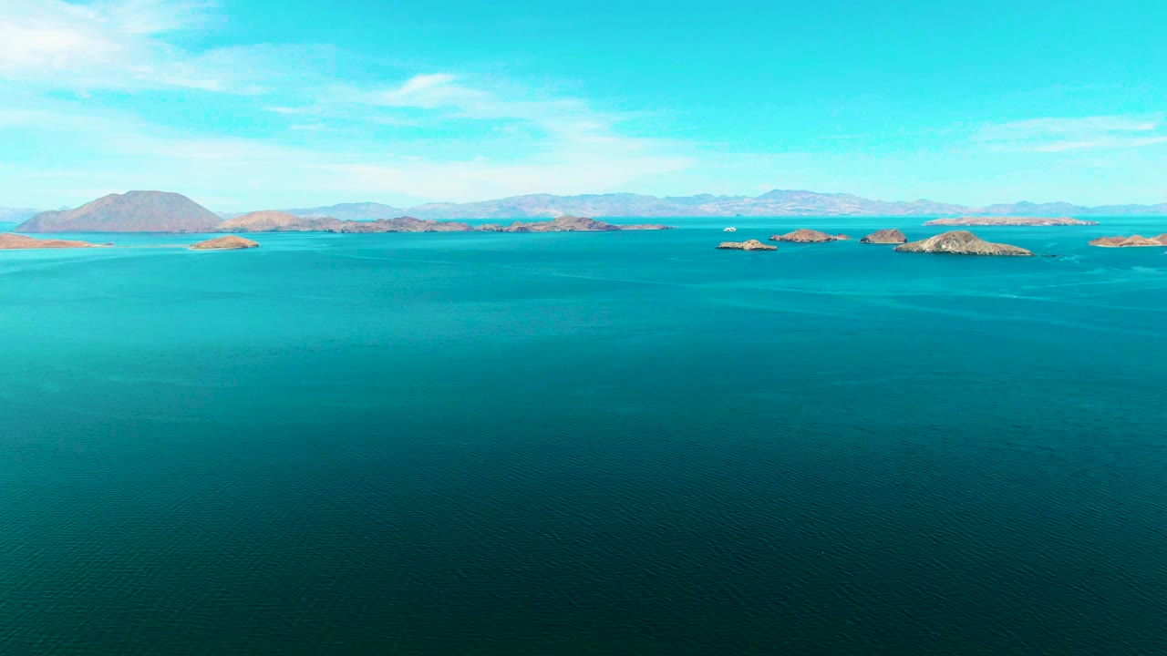 Second frame holds on Bahia De Los Angeles water with deep blue foreground, turquoise shallows near the islands, a rounded island mass to the left, and no visible people.
