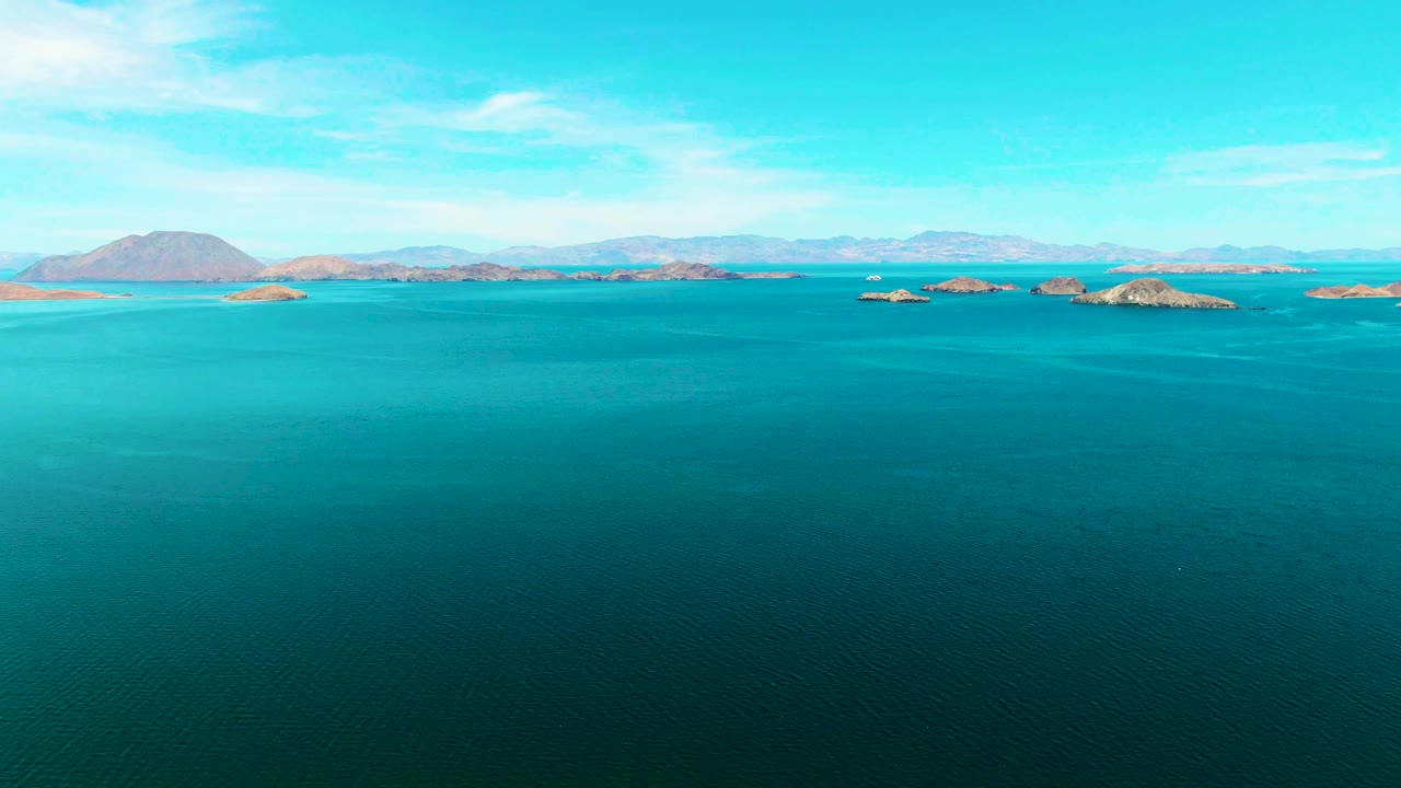 Aerial ocean view with turquoise shallows and rocky islands along the horizon.