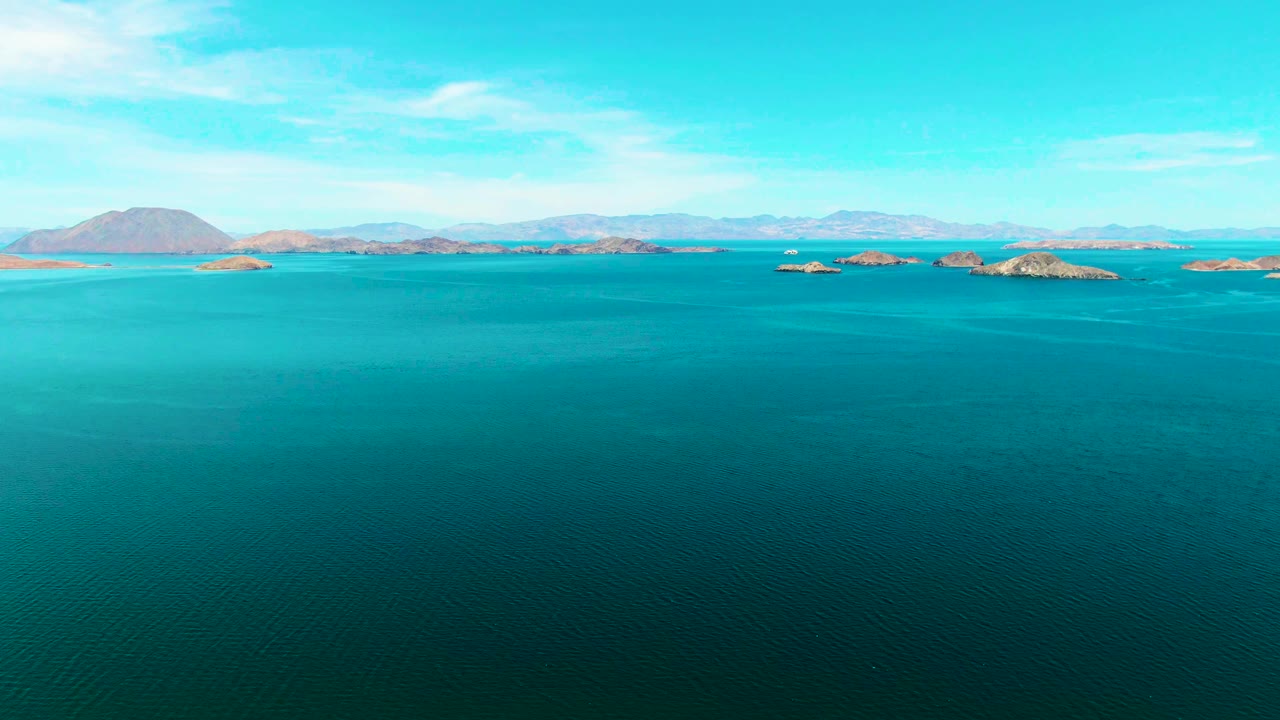 Turquoise ocean with distant rocky islands and mountains under a bright sky