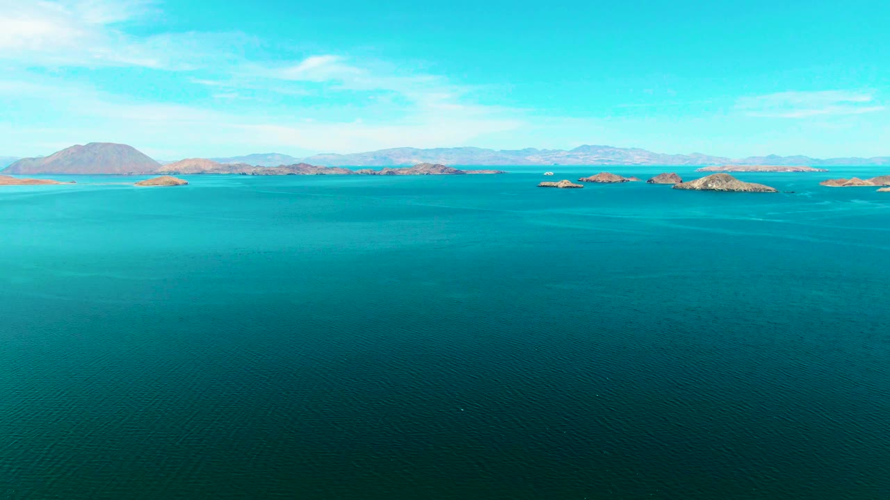 Aerial frame of calm blue-green sea in Bahia De Los Angeles, with scattered rocky islands across the midground and no visible people.
