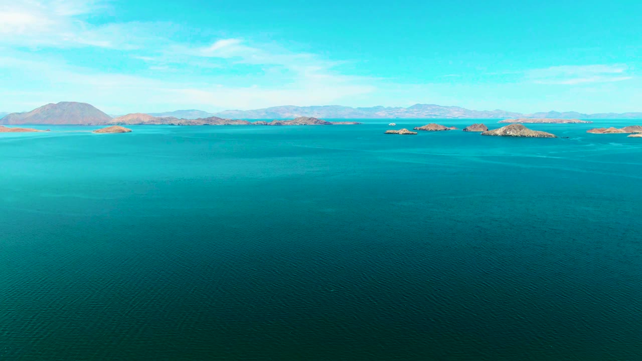 Open turquoise water stretches toward rocky islands and pale mountains in Bahia De Los Angeles, with a bright sky above and no visible people.