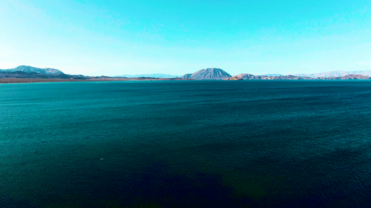 Wide blue water with distant mountains under a clear sky.