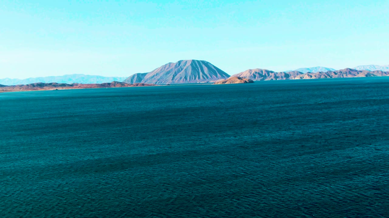 At 0:00 in Bahia De Los Angeles, deep blue water fills most of the frame with a low mountain coastline on the horizon and no visible people.