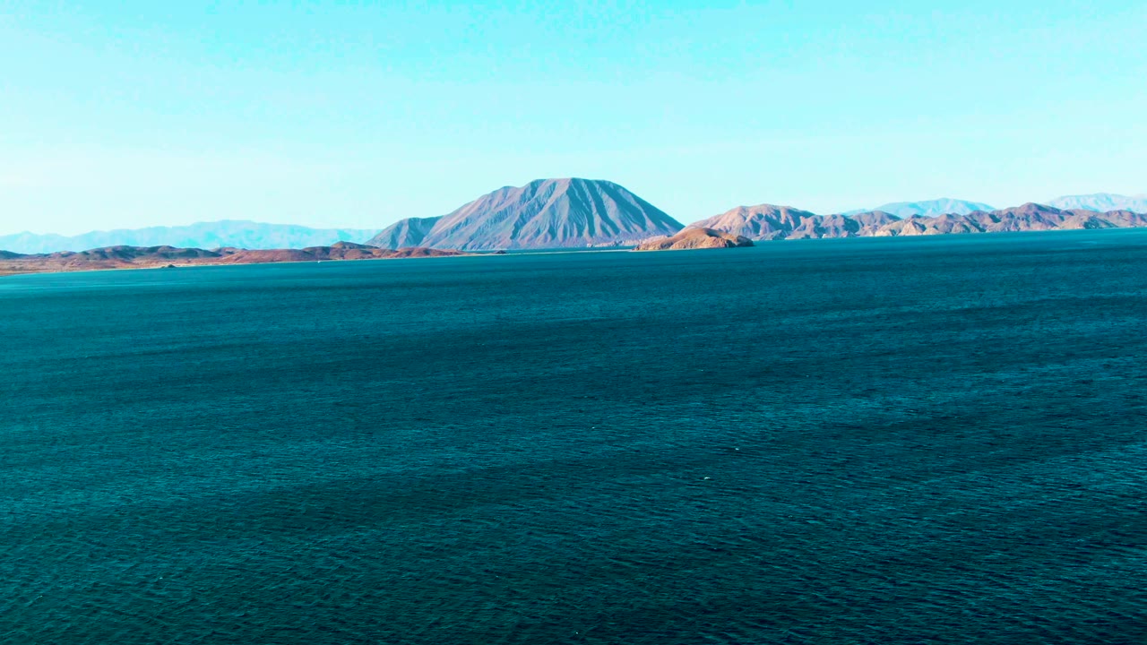 At 0:01, the Bahia De Los Angeles coastline remains distant across the top of the frame while textured blue water dominates the foreground and no visible people appear.