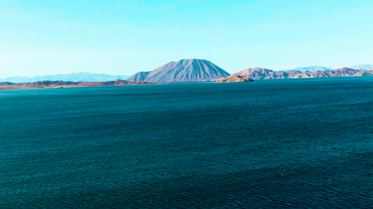 Wide aerial view over blue water toward a distant mountain island in Bahia De Los Angeles, Mexico, with no visible people.