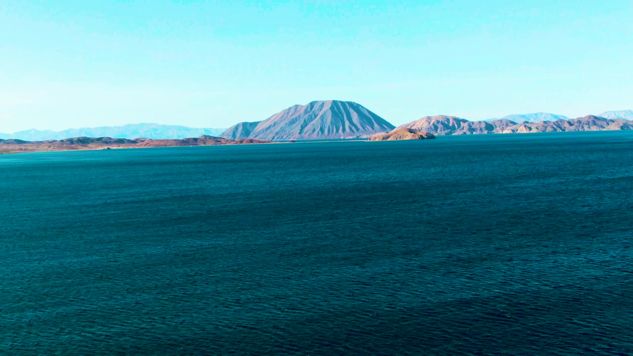 Blue ocean ripples fill the lower frame while rugged island mountains sit across the horizon in Bahia De Los Angeles, Mexico, with no visible people.