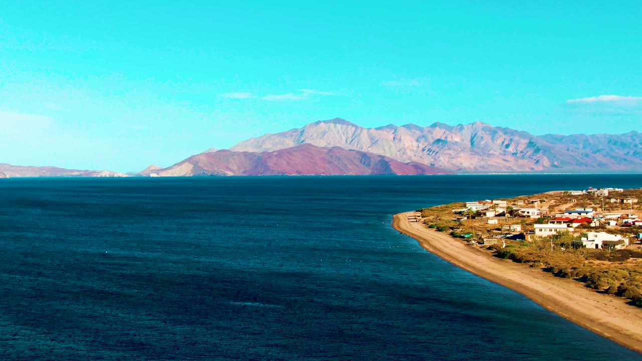 Bahia De Los Angeles shoreline holds along the right side while rippled blue water fills the foreground and pale mountains sit under a clear sky, with no visible people.