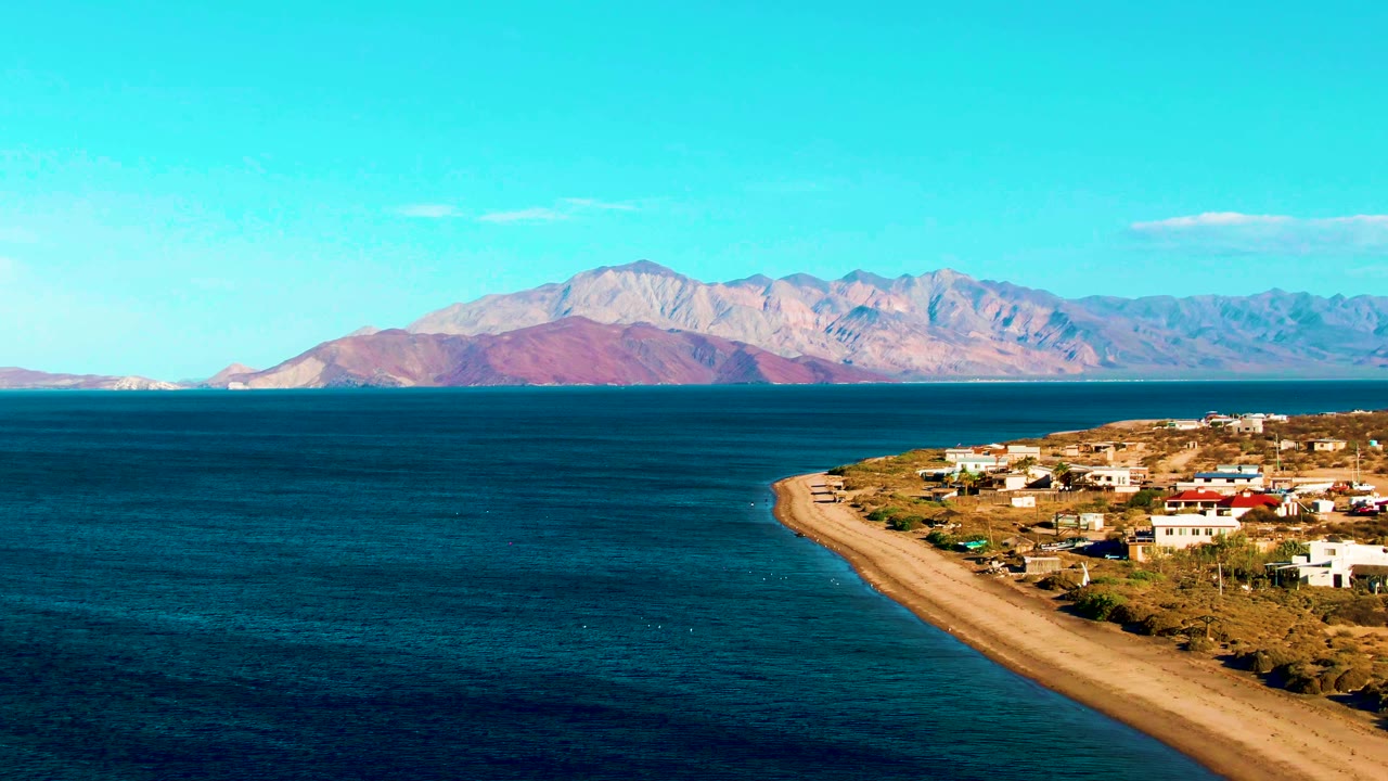 Coastal settlement beside a narrow sandy beach and calm blue water.
