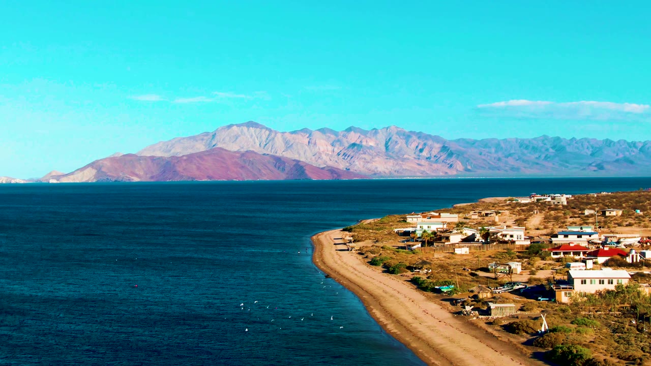 Ocean foreground with shoreline buildings, road, boats, and mountains