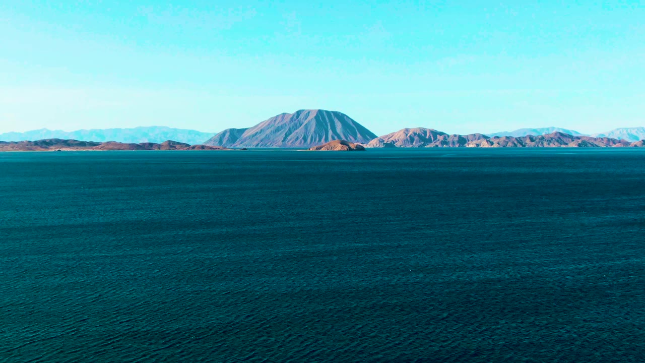 Opening frame of Bahia De Los Angeles showing broad dark turquoise water, a distant brown and gray mountain range, clear blue sky, and no visible people.