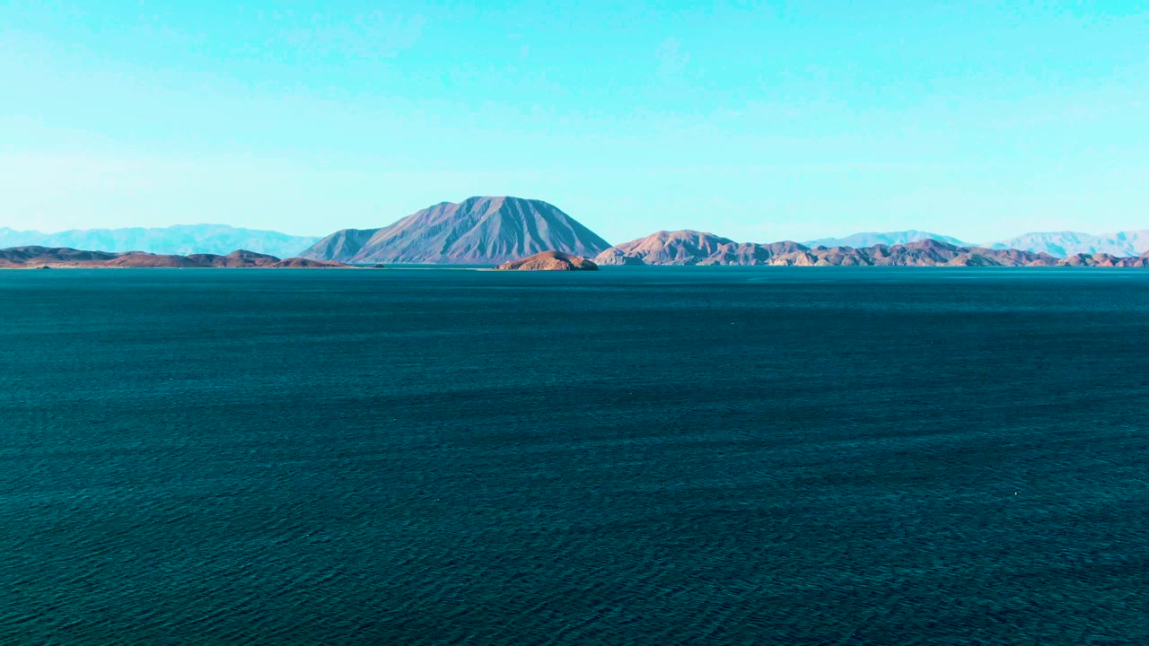 Wide blue ocean with distant mountains under a clear sky.