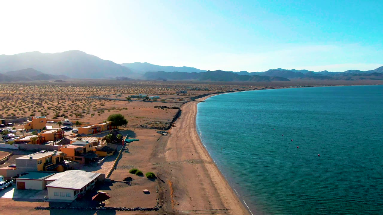 Elevated coastal view with buildings near the beach and turquoise water along the shore.