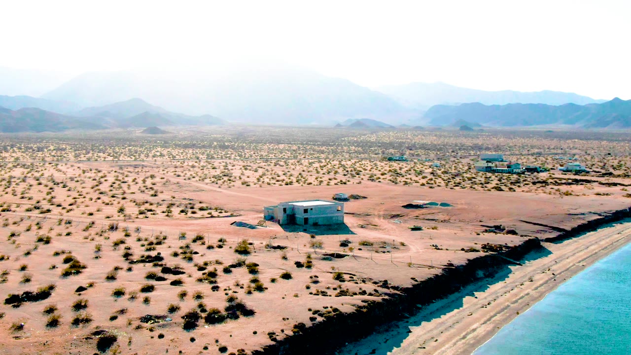 Aerial view of desert shoreline with water at lower right and mountains in haze.