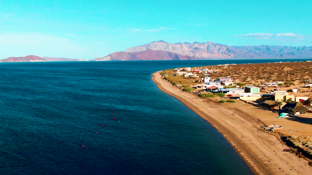 Wide aerial view of calm ocean beside a sandy developed shoreline and mountain backdrop