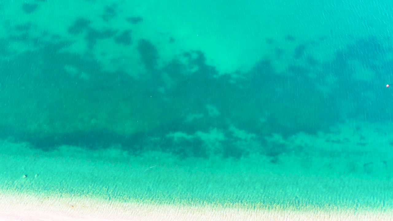 Clear turquoise water over pale sand and dark underwater patches.