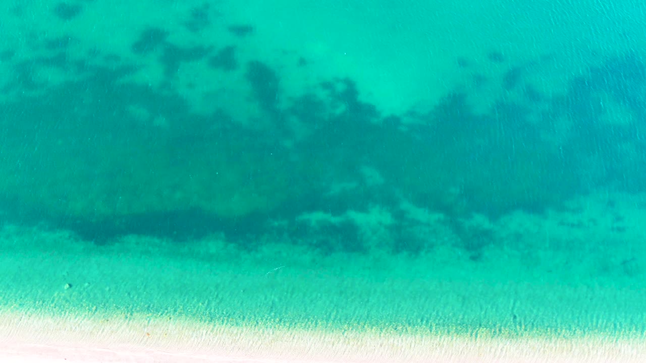 Clear shallow water in Bahia De Los Angeles, Mexico, shows a pale sandy bottom with a darker submerged band crossing the upper frame and no visible people.