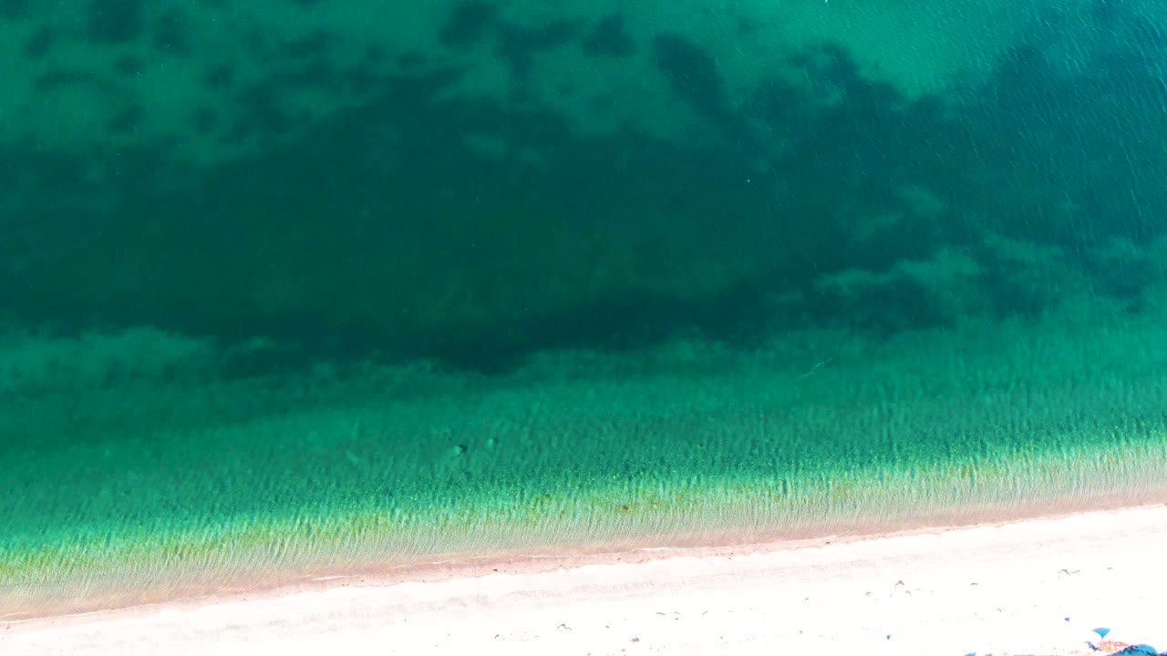 Turquoise shallows and sandy beach viewed from directly above.