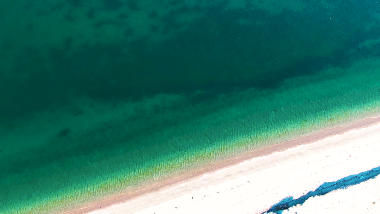 Aerial shoreline with dark water patches and pale sand.
